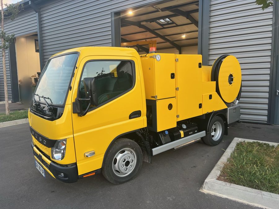 Camion hydrocureur jaune de LLB Service devant l'atelier